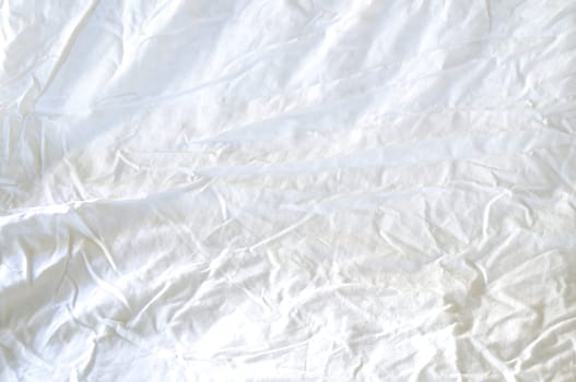 A large white rumpled and wrinkled sheet fills the frame lit with morning light.