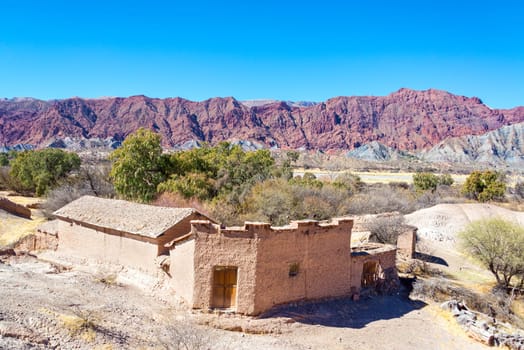 Rustic old building made of adobe with dramatic red hills rising in the background in the small town of Chacopampa near Tupiza, Bolivia