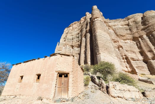 Rustic adobe building at the base of a dramatic cliff in the small town Espicaya near Tupiza, Bolivia