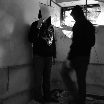 Man holding glass fragment and blurry figure with sunlight reflected from broken window. Black and white.