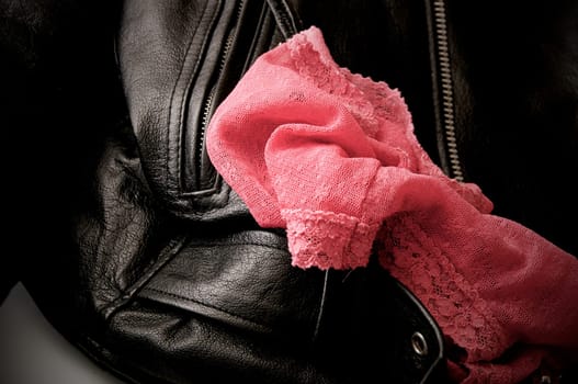 A pair of woman's pink lace panties is draped upon a man's black leather jacket.