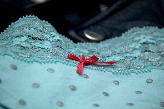 A pair of woman's blue polka dot lace panties with pink bow is draped upon a man's black leather jacket.