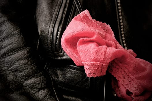 A pair of woman's pink lace panties is draped upon a man's black leather jacket.