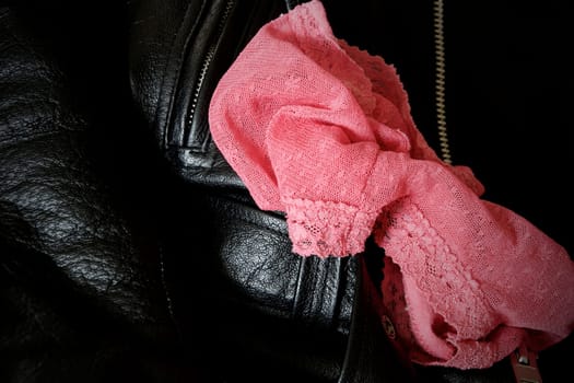 A pair of woman's pink lace panties is draped upon a man's black leather jacket.