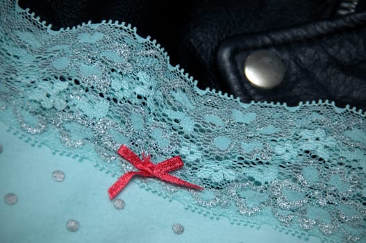 A pair of woman's blue polka dot lace panties with pink bow is draped upon a man's black leather jacket.