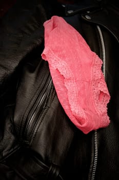 A pair of sexy woman's pink lace panties is draped upon a man's black leather jacket.