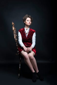 Portrait of beautiful Caucasian model in red Victorian-style velvet dress, seated on wooden chair