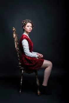 Portrait of beautiful Caucasian model in red Victorian-style velvet dress, seated on wooden chair