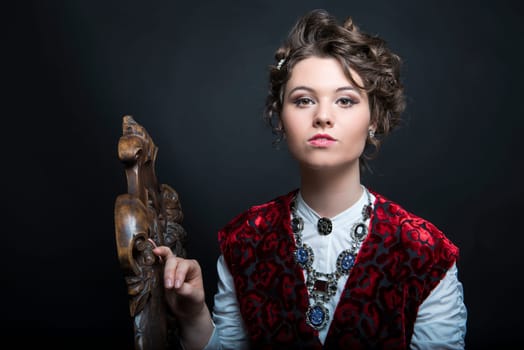 Portrait of beautiful Caucasian model in red Victorian-style velvet dress, seated on wooden chair