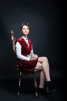 Portrait of beautiful Caucasian model in red Victorian-style velvet dress, seated on wooden chair