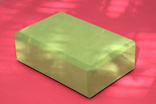 A green yoga block on a pink yoga mat with dappled sunlight adding depth and texture to the image.