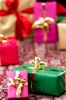 Green gift box between other plain-colored presents wrapped in magenta, gold and red. Tight close-up shot with shallow depth of field.