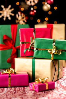 Stack of plain presents in red,green and gold placed on a festive cloth. Orange light reflexes,blurred stars and baubles in the back. Seasonal background for Xmas.