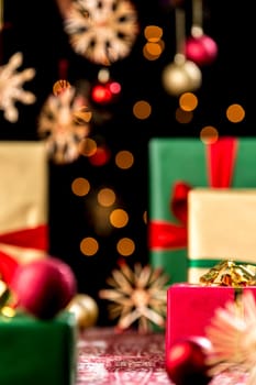 Sparkling Christmas gift setup. Golden twinkles and blurred stars against black background. Red gift box is in focus. Green and golden presents are unsharp.