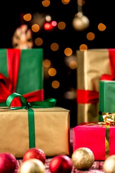 Plain Christmas gifts with bows in gold,red and green. Baubles in front. Golden twinkles over black background. Shallow depth of field.