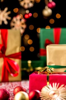 Red gift box amidst Christmas baubles and straw stars. Behind,plain presents in gold and green. Twinkles and blurred stars in the back. Shallow depth of field.