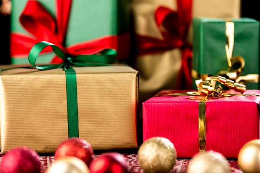 Presents with bows wrapped in green,gold and red. Tightly-framed close-up. Christmas ornaments out of focus. Red gift within depth of field.