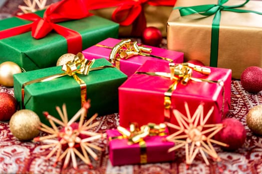 Christmas gifts wrapped in red,green and gold with plain-colored bows amidst baubles and straw stars. Tightly-cropped shot with focus on magenta gift box in center.