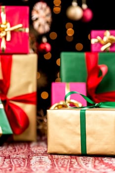 Plain Christmas gifts in gold,magenta,green and red piled up. Golden gift with green bow is within narrow depth of field. Orange twinkles,blurred baubles and stars against pitch black.