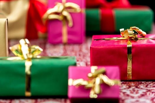 Red gift with golden bow knot amidst other plain presents clad in magenta, green and gold. Tightly-framed background for any gift-giving occasion.