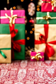 Christmas presents piled-up on a festive cloth. Wrapping and ribbons in gold, red, magenta and green. Twinkles and blurred stars in the back. Plenty of text space in void foreground.