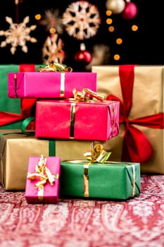 Pile of Christmas gifts wrapped in red,gold,green and magenta. Shallow depth of field. blurred stars,baubles and twinkles in the back. Xmas background with text space.