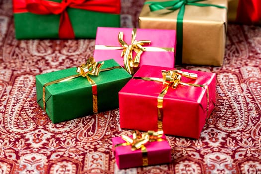 Plain presents in red,magenta,green and gold placed on a festive cloth. Unicolored ribbons and bows. Focus is set on the small green gift with golden bow knot.