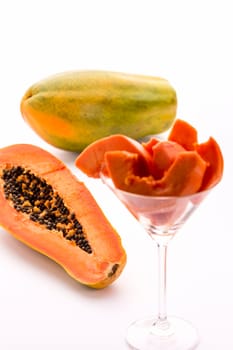 A halved and an entire papaw fruit. Slices of its fruit flesh arranged in a drinking glass..