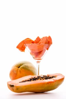 Vibrant tangerine slices of the papaya fruit presented in a cocktail glass against a white background and a halved fruit in front..