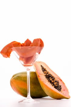 A halved papaya leaning against the globose body of an entire fruit. The ripe pulp has a vibrant tangerine color and numerous black seeds reminiscent of black pepper..
