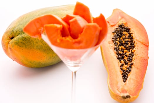 Fruit flesh of the papaya arranged in a glass,but the focus rests on the halved papaya and entire fruit in the back..
