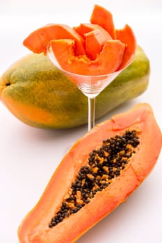 The oblong shape of half a papaya and its fruit flesh in a glass. The depth of field is running across both the papaya slices and the pulp revealed by the longitudinal section of the halved fruit..