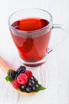 Fruit red tea with wild berries in wooden spoon on white wooden table