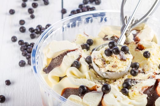 Vanilla and chocolate ice cream with blackberry scoop scooped out of a container on white wooden background