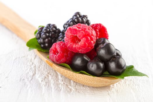 Fresh berries in wooden spoon on white wooden table