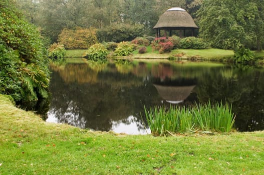 Landscape view of a small tech with reflection of the pavilion behind it in autumn