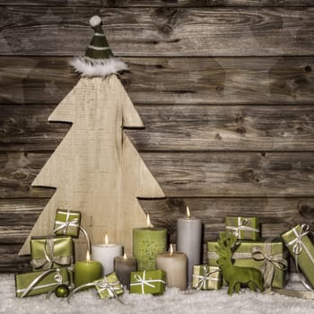 Natural christmas decoration in green and brown on wooden background with presents and burning candles.