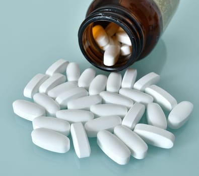 White large pills and glass bottle on blue background