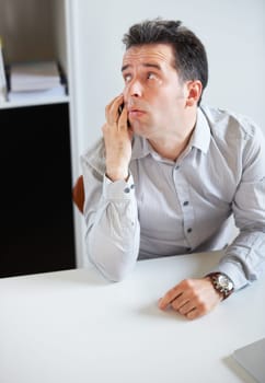 Phone call, thinking or waiting with a business man sitting at his desk in the office for work. Time, contact and communication with an impatient young employee talking on his mobile in the workplace.