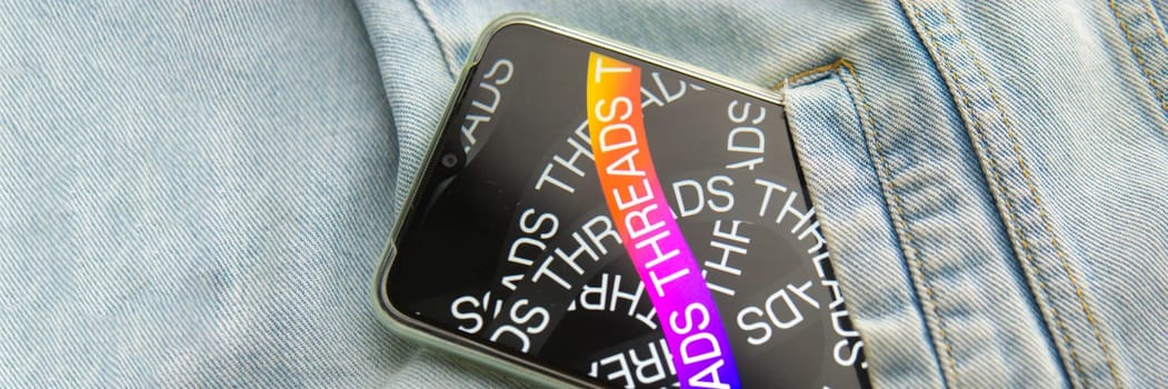 Tver, Russia - July 15, 2023, the threads logo on the smartphone screen lying on the jeans. The threads icon. The logo of the current application. Threads social network