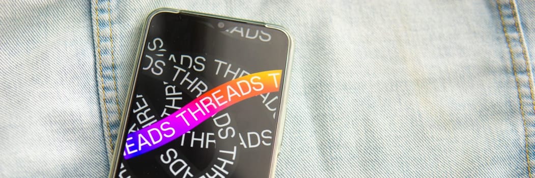 Tver, Russia - July 15, 2023, the threads logo on the smartphone screen lying on the jeans. The threads icon. The logo of the current application. Threads social network