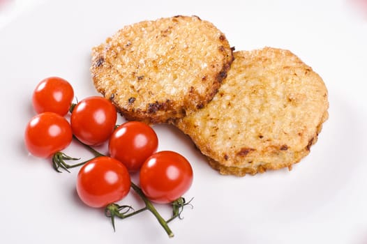 Two cutlets with branch of small tomatos on white plate