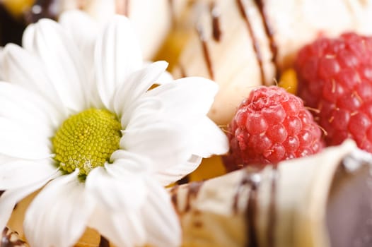 Piece of cake on plate with berries and fruits and camomile