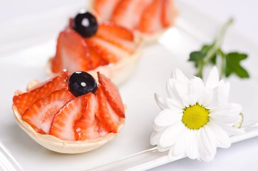 Piece of cake on plate with berries and fruits and camomile