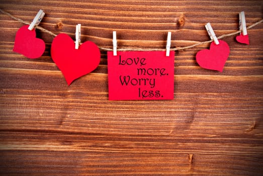 The Saying Love More Worry Less on a Red Label with Hearts Hanging on a Line on a Wooden Background