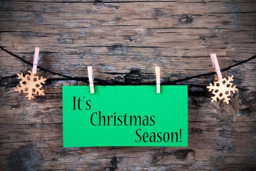 A Green Label with Its Christmas Season on it, Hanging on a line on wooden Background