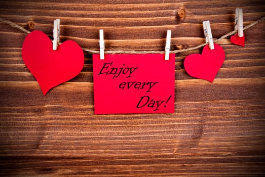 The Saying Enjoy every Day on a red Label with Hearts Hanging on a Line on a Wooden Background