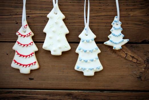 Four Christmas Tree Cookies with different Decorations Hanging on a Wooden Background