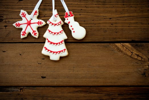 Three Red and White Christmas Cookies Hanging on White Ribbons with Wood as Background with Copy Space