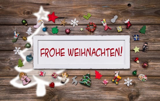 Greeting card for christmas with german text for merry christmas. Colorful decoration with miniatures and a white wooden sign.